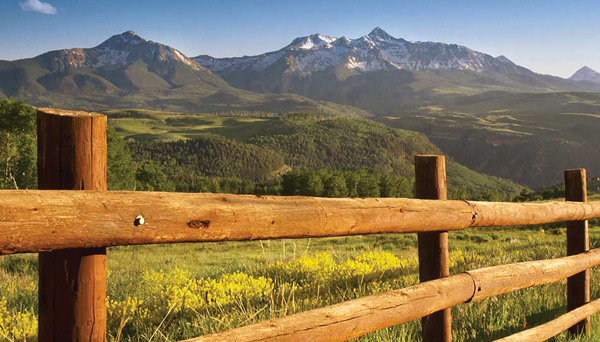 fence traversing field with mountains in the background