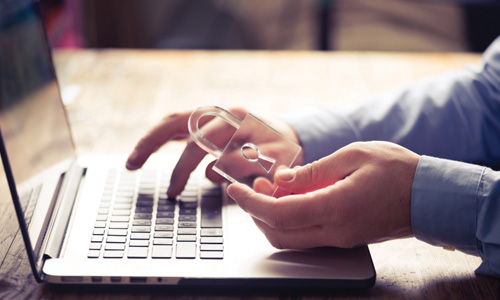 person using a laptop while holding a padlock paperweight